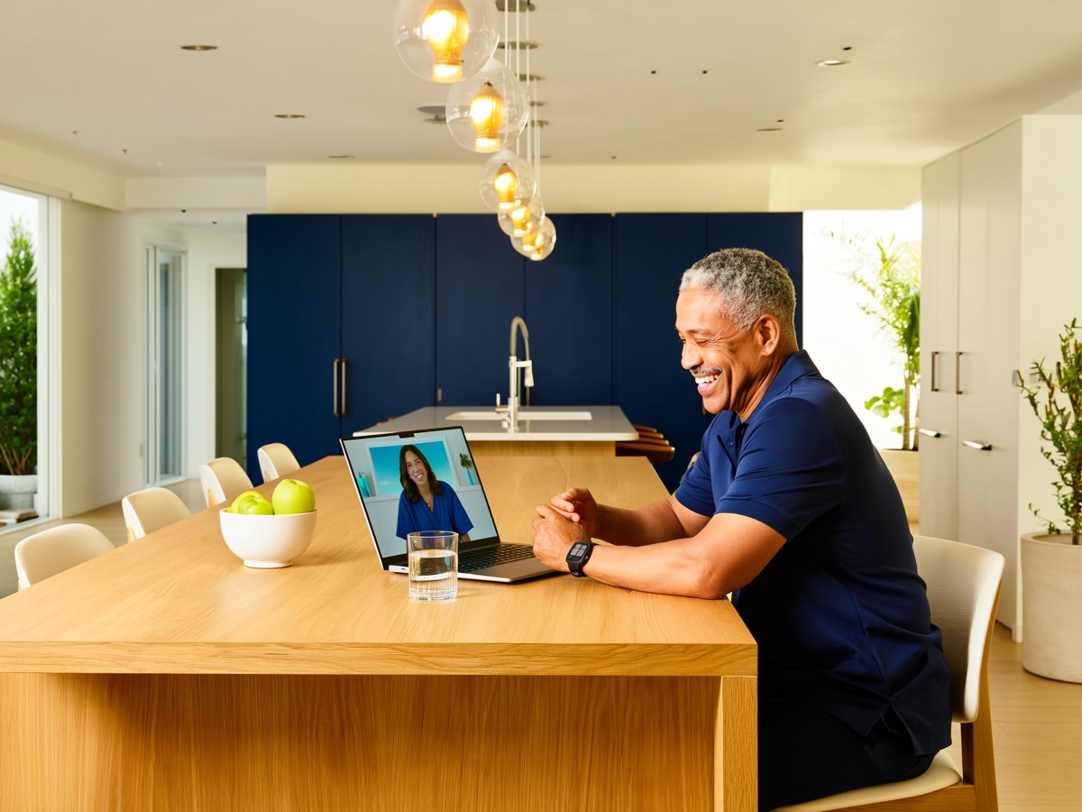 A man at his kitchen table on a video call, laptop facing away